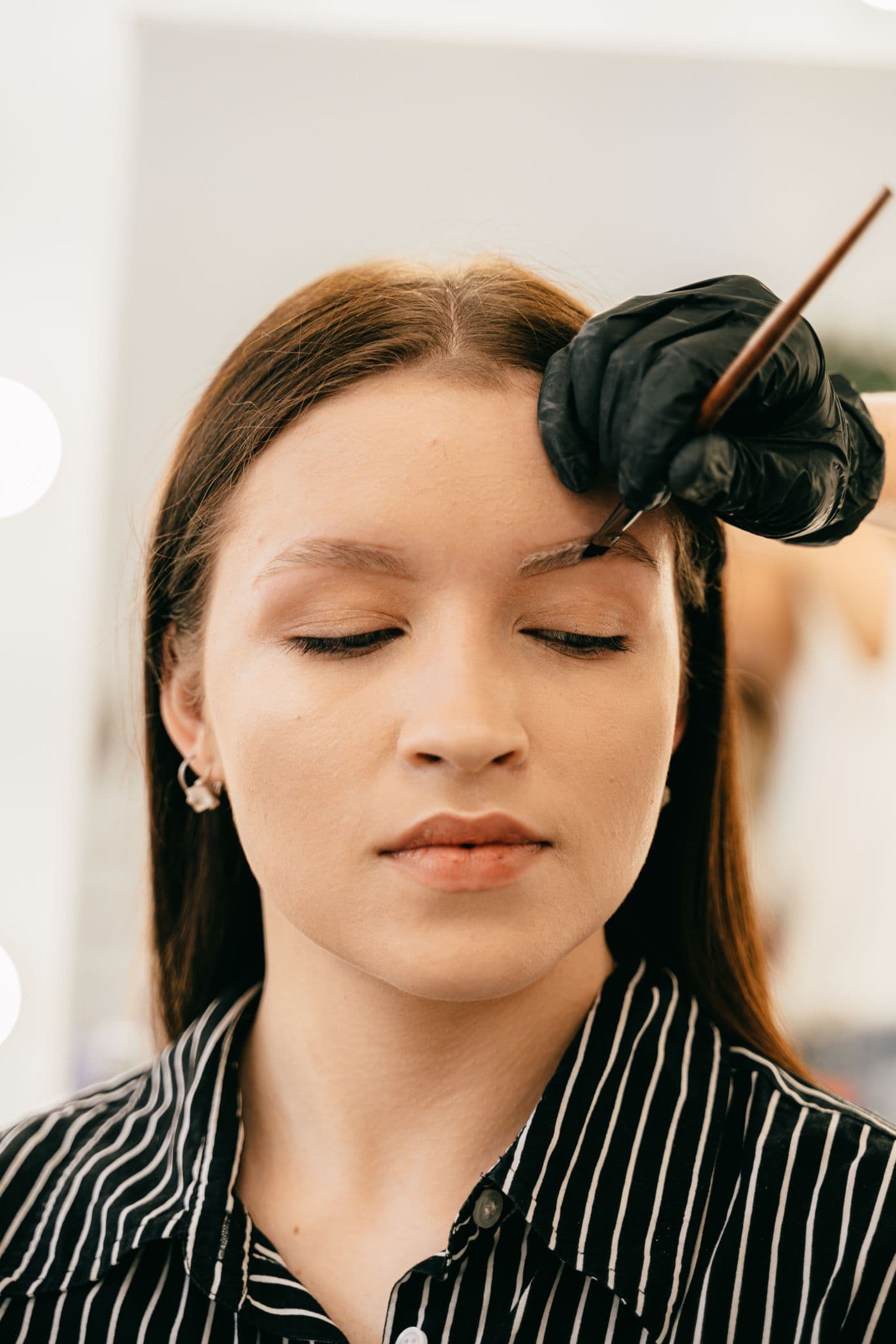 A brow artist applying a treatment solution to a client's eyebrows during a salon appointment